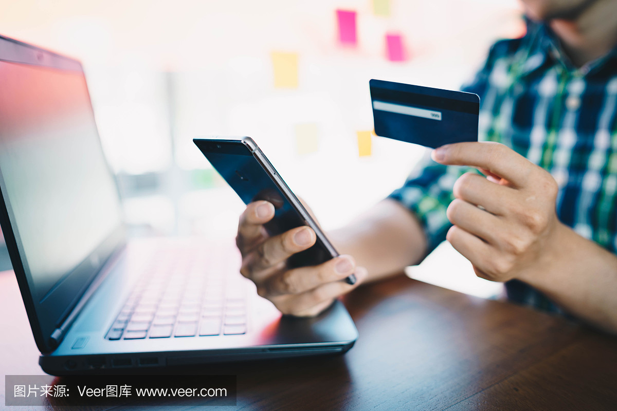 男人用手机和笔记本电脑通过信用卡在网上购物。支付购买。网上购物,网上支付,购买和销售产品和服务。